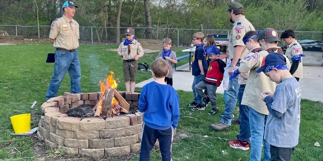 Cub Scouts and leaders gathered around a brick fire ring