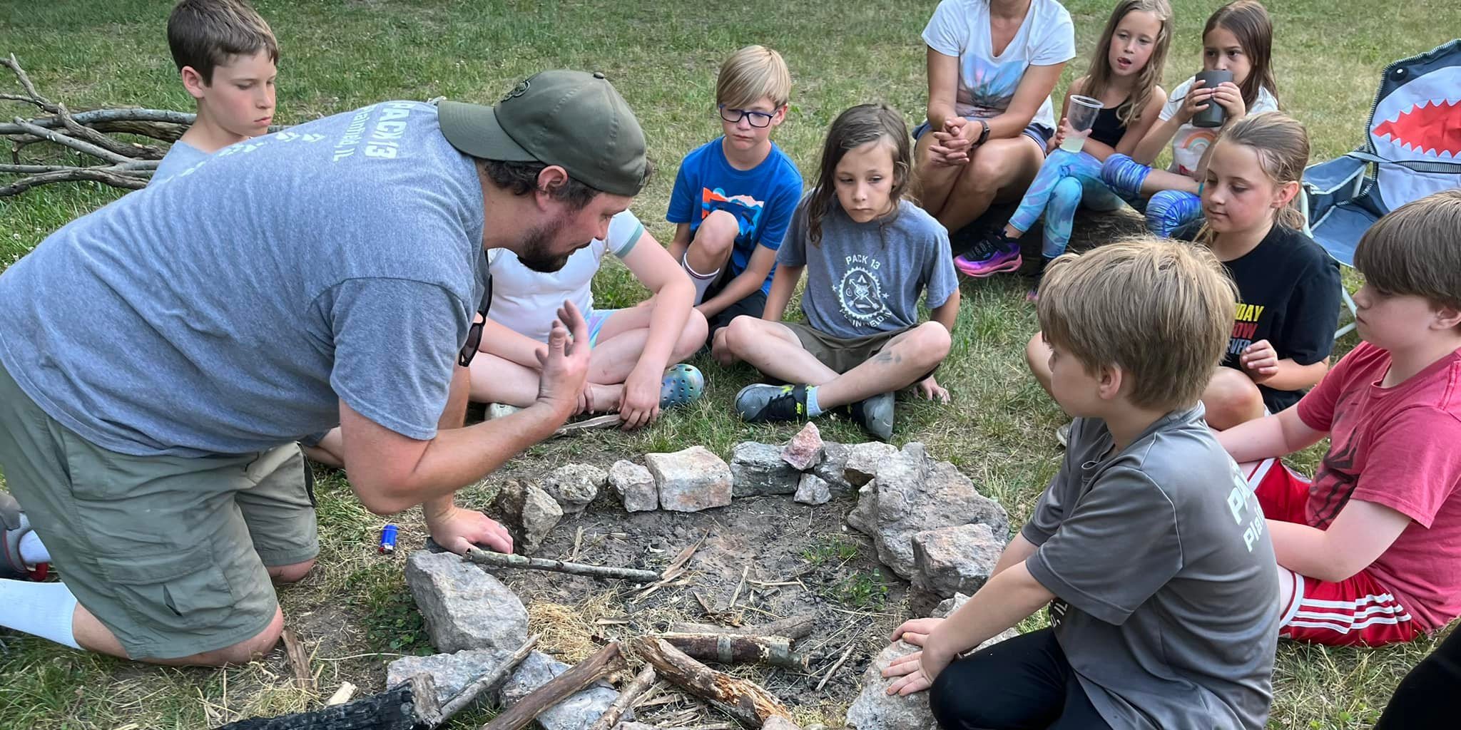 Scouts and a leader laying sticks inside a stone fire circle