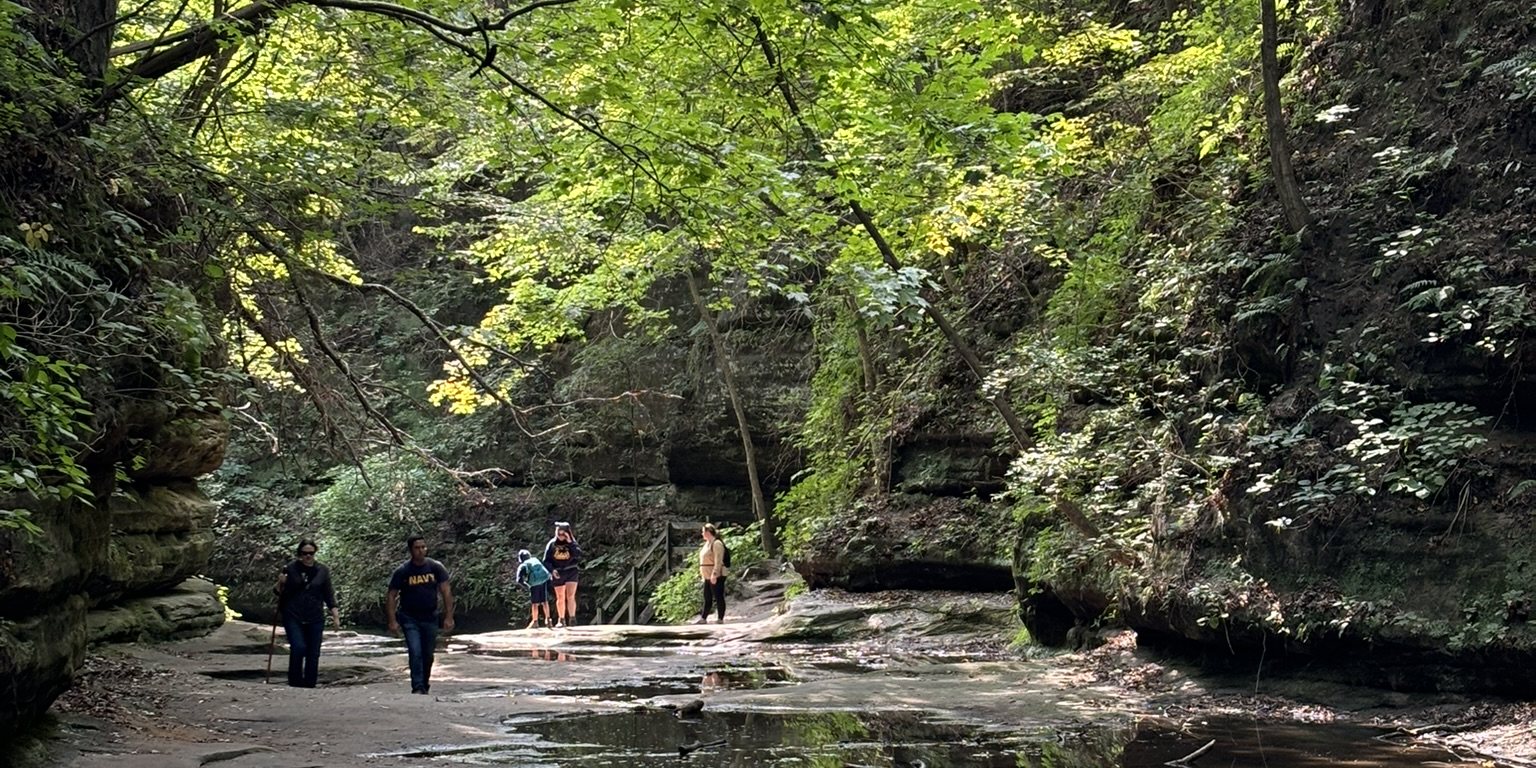 Pack families walking a canyon trail beside still water at Starved Rock